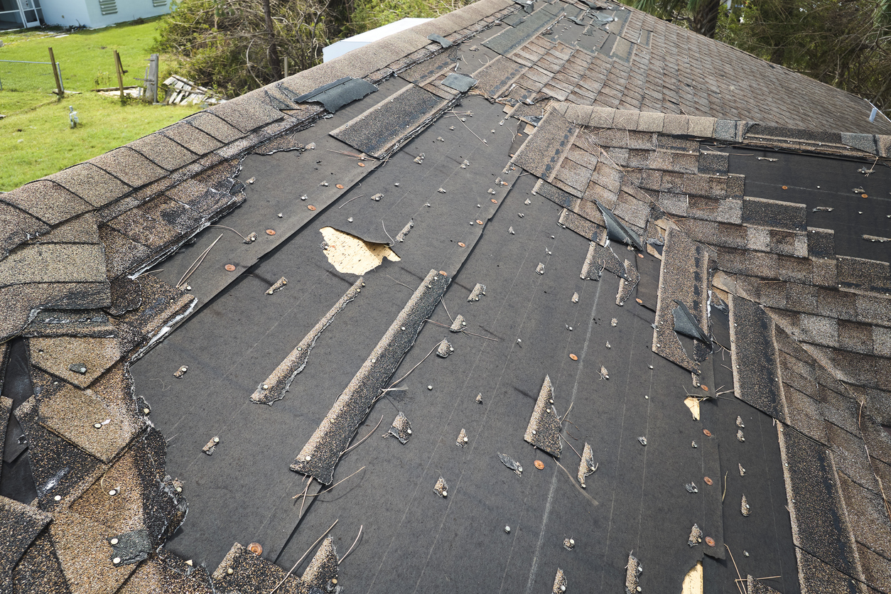 Wind damaged house roof with missing asphalt shingles after hurricane Ian in Florida. Repair of home rooftop concept