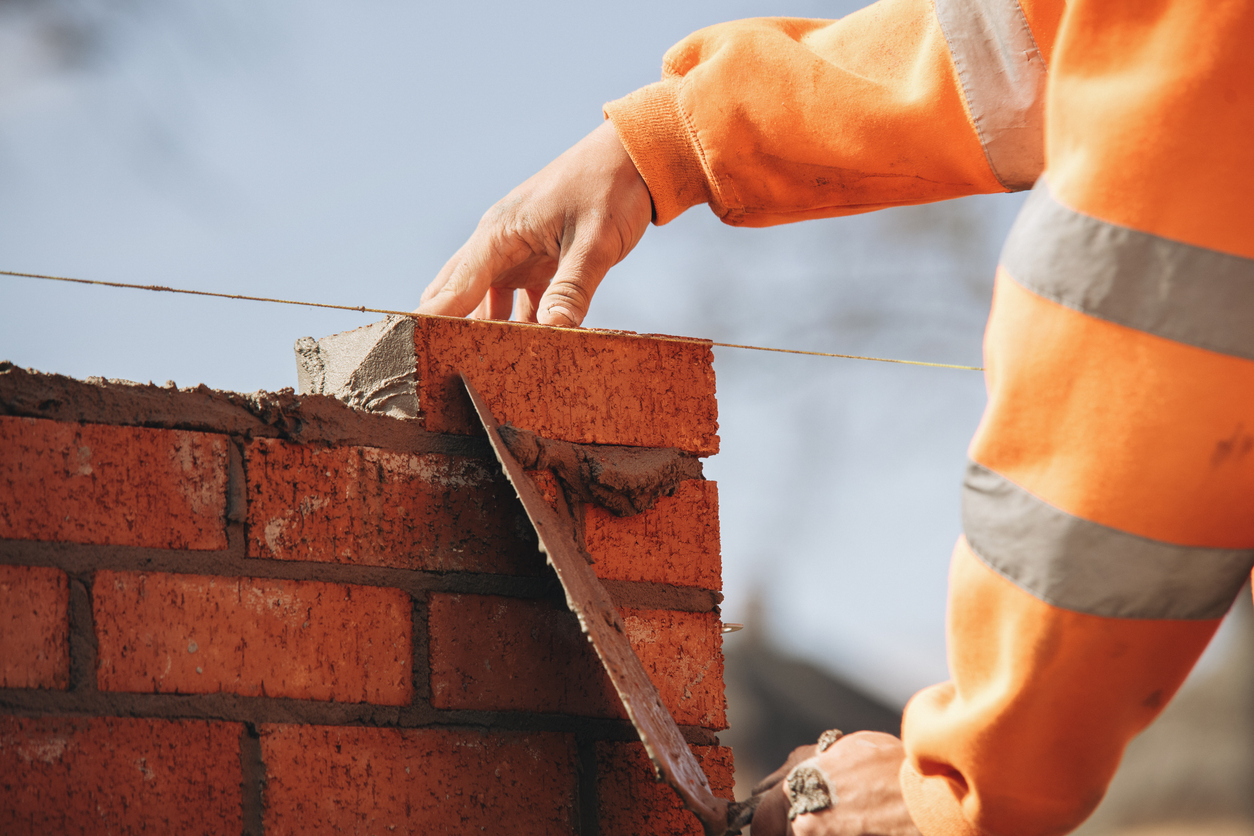 Close-up of skilled bricklayer working on construction site laying one more red brickin the wall